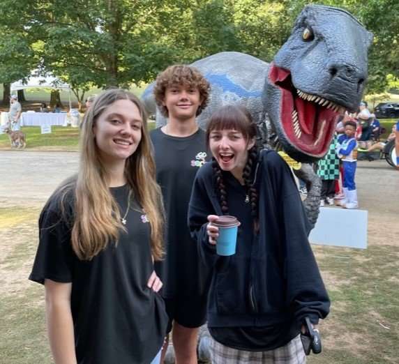 Three kids standing in front of a dinosaur.