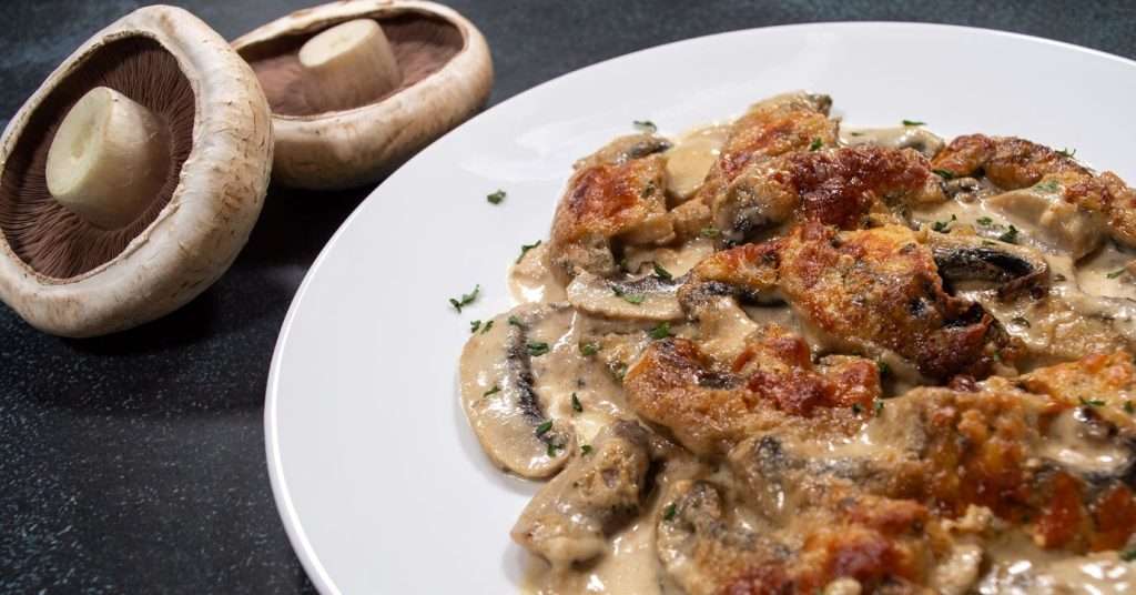 Scalloped mushrooms on white plate with white mushroom next to it.