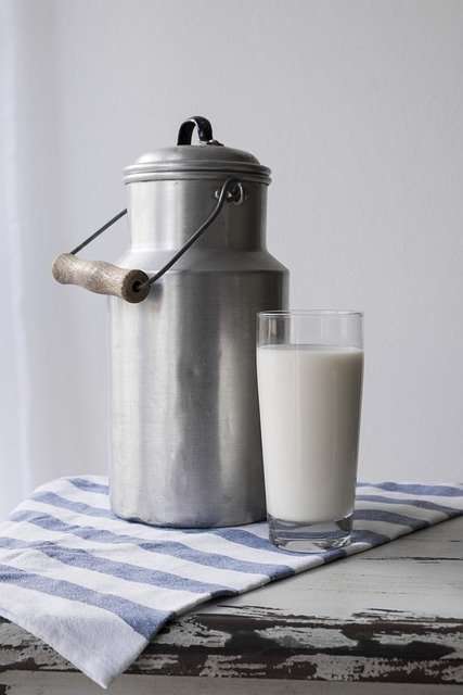Stainless steel milk jug and a glass of milk on a table. 