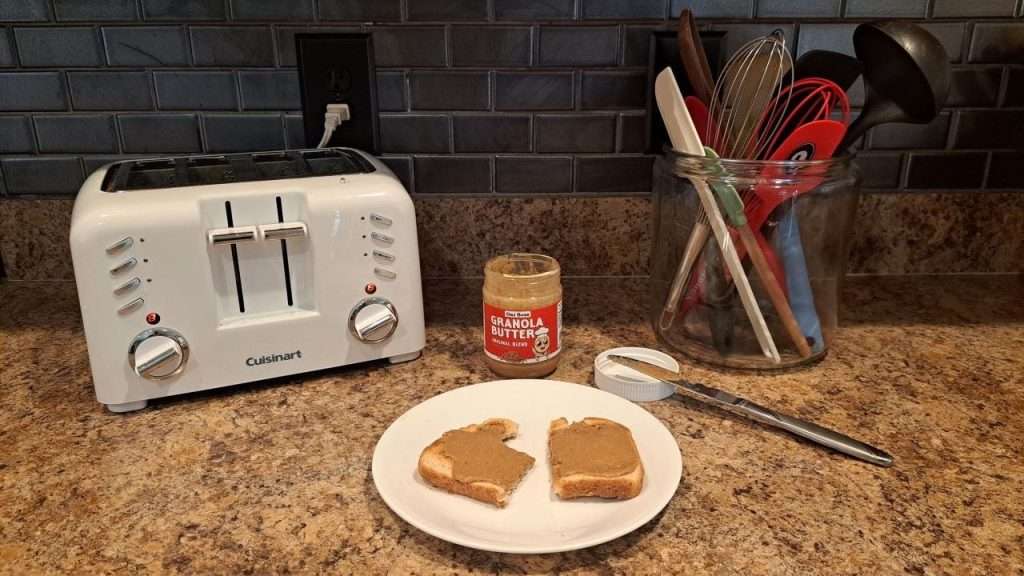 Granola spread on toast with toaster and utensils in background.