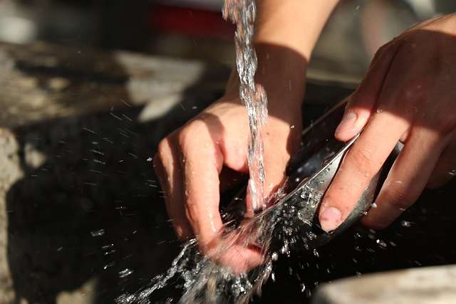 Hands washing a bowl under running water.