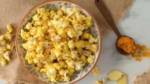 Popcorn in a bowl with turmeric spice in a measuring spoon on placemat.