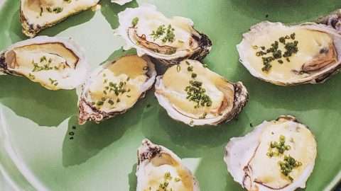 Roasted Oysters On A Half Shell with cream and chives on a green plate.