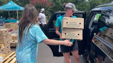 Volunteers loading food box produce into a vehicle. 