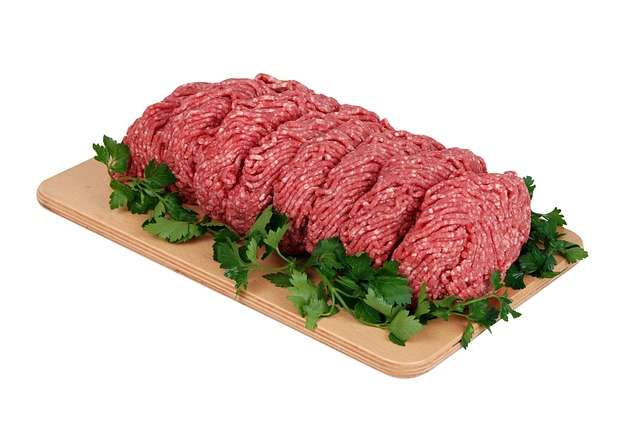Raw ground beef on cutting board with garnish around it. 