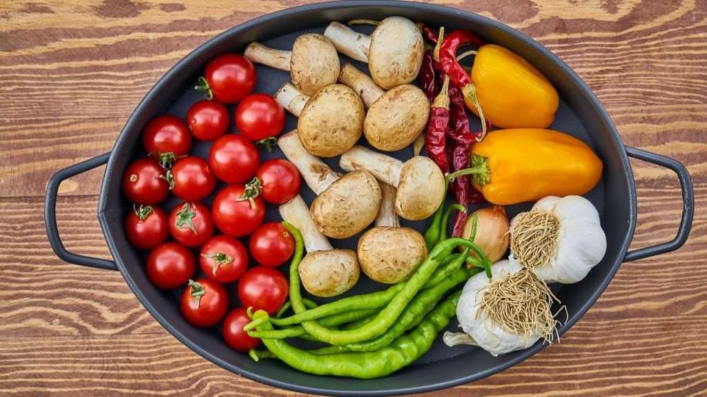 Pan displaying healthy food choices: tomatoes, mushrooms, assorted peppers, green beans and garlic.