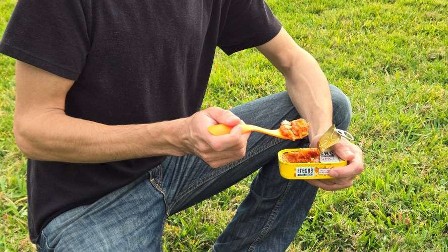 Man in black shirt and jeans holding a fork full of Freshe meal coming out of the can.