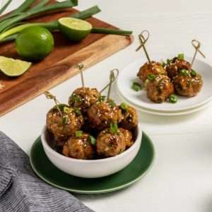 Turkey meatballs in a bowl with toothpicks next to a cutting board with lime and chives.