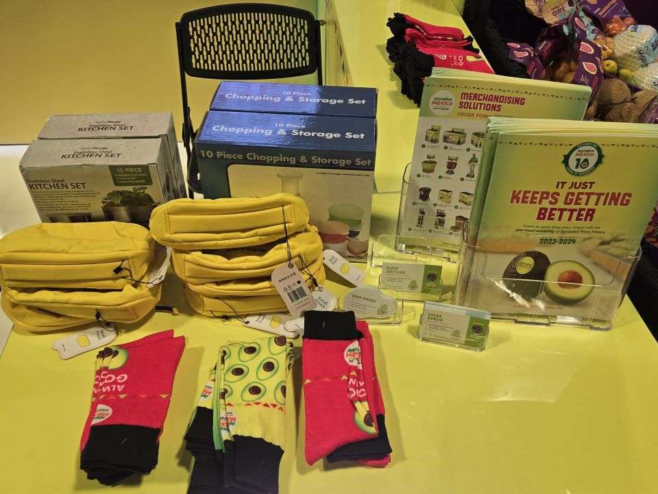 Avocados From Mexico display - socks, fanny packs, literature and kitchen equipment on yellow cloth.
