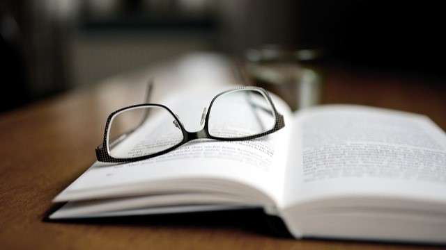 Eye glasses sitting on open book on a table.