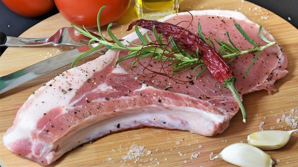 Raw pork chop prepped for the grill with rosemary, salt, pepper, and a chili pepper.