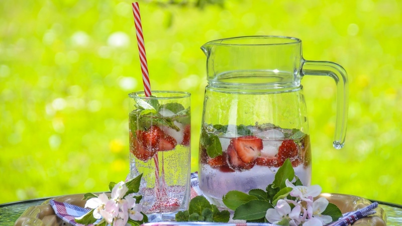 A glass and pitcher of water flavored with fresh strawberries and mint.