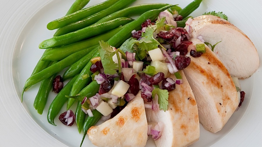 Grilled chicken plated with green beans and cranberry salsa topping. 