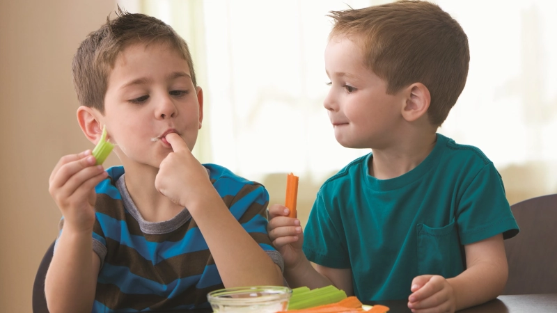 Two kids eating carrot sticks.