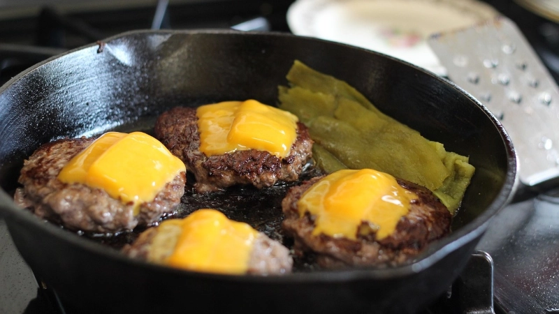 Burgers topped with cheese cooking in a cast iron skillet.