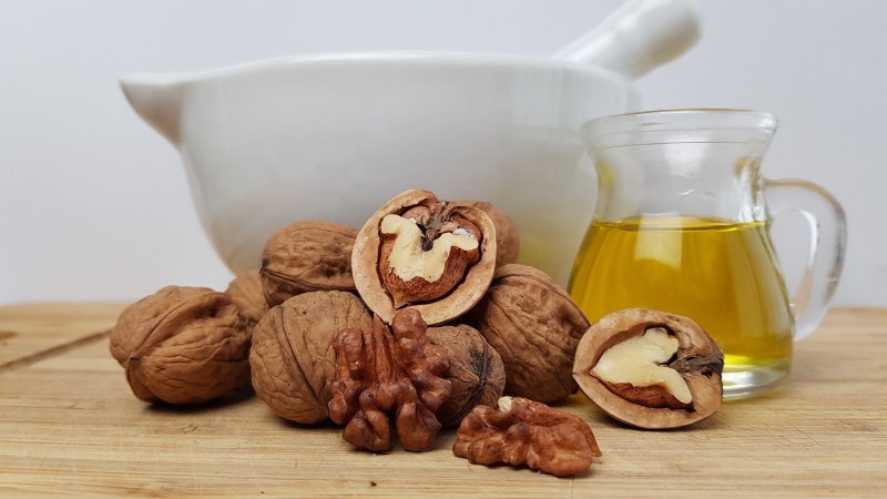 Walnuts on a table with a small pitcher of olive oil.