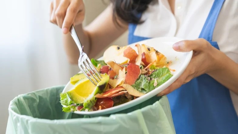 Scraping food off plate into a garbage.