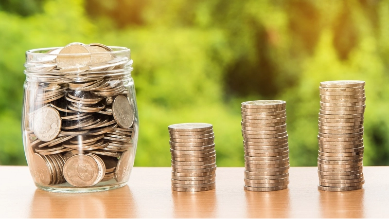 Jar full of coins next to three stacks of coins. 