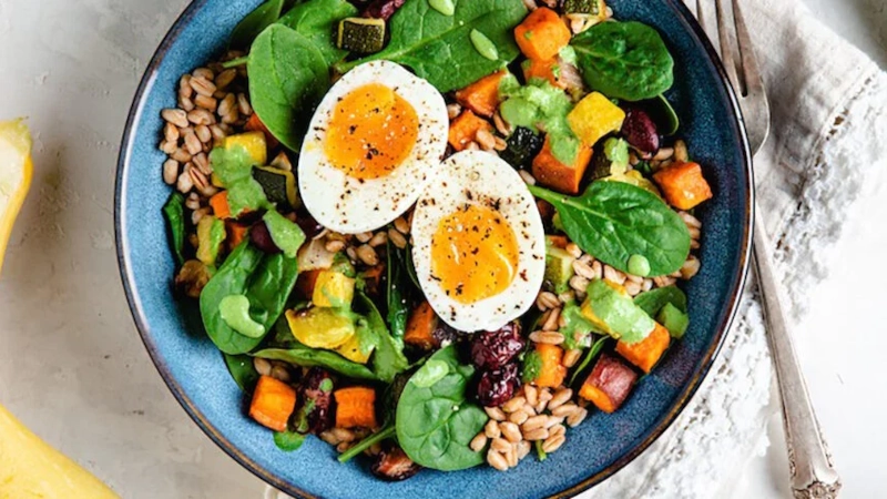 Spinach salad with egg, sweetpoatoe, sunflower seeds, and raisins.