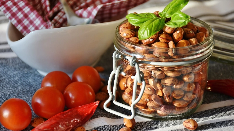 Jar of dried pinto beans on table with cherry tomatoes and a red chili pepper. 