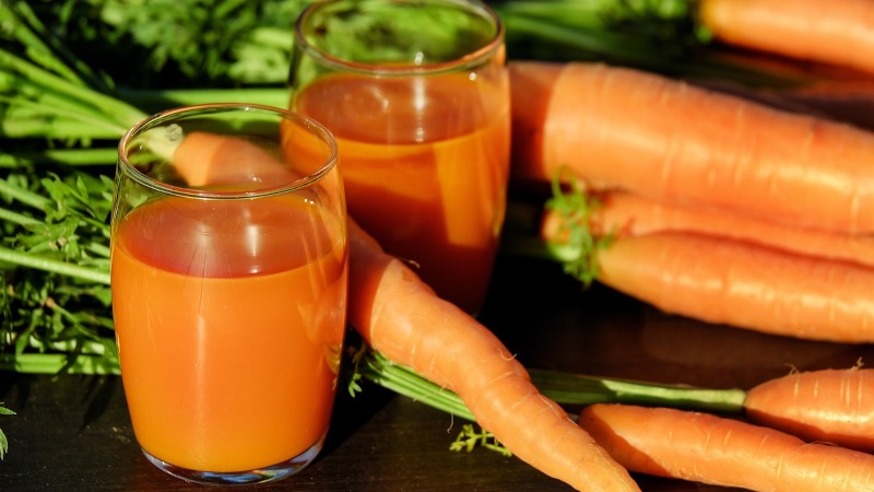 Carrots on table with glasses of carrot juice. 