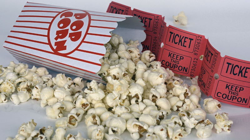 Cardboard container of spilled popcorn with red movie tickets.