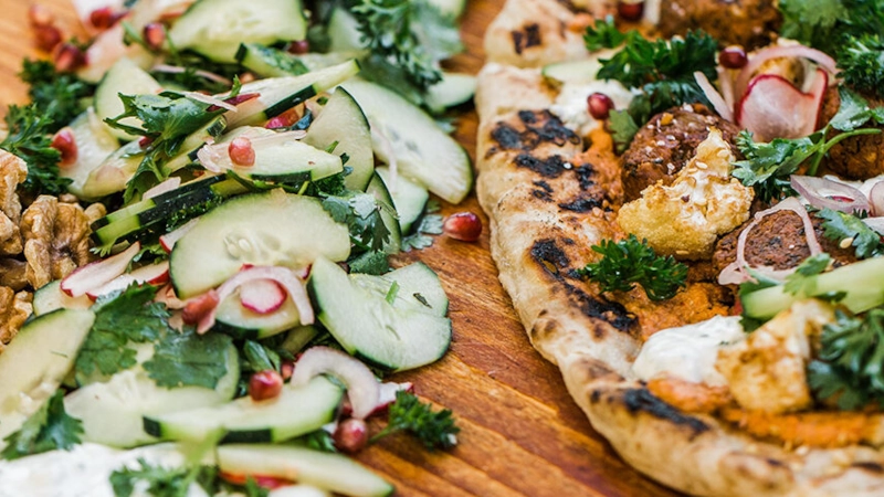 Walnut Falafel Flatbread with Red Pepper Walnut Tahini with cucumber and onion on the side.