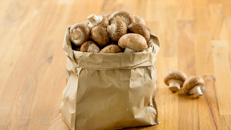 Bag full of Crimini mushrooms on a table top.