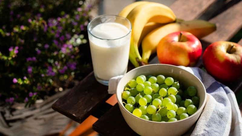 Bowl of graps, bananas, apples and a glass of milk.