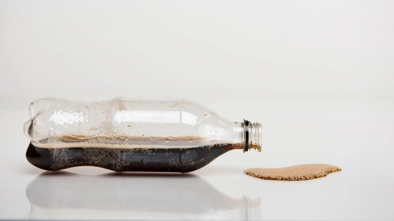 bottle of soda on it's side dripping onto table top.