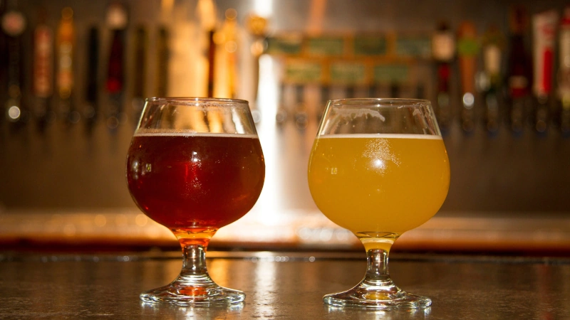 Two snifter glasses of beer on a bar.