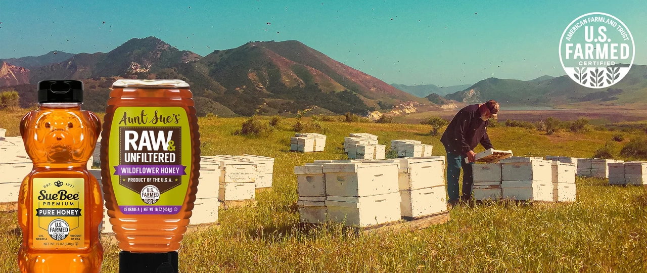 Bottles of Sue Bee and Aunt Sue's honey in front of bee hives. 