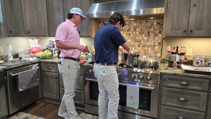 Jake watching Luke stirring a pot in front of stove. 