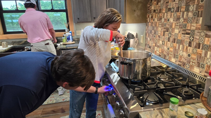 Luke adjusting flame and Lana stirring pot in front of stove.