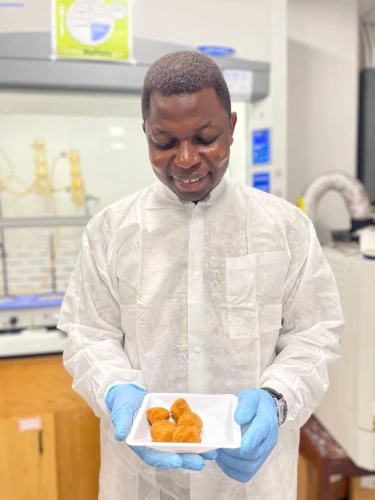 William Oyom in the lab holding a plate of fried foods.