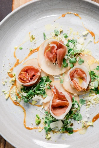 Che Vita's Arugula & Prosciutto Salad garnished with honey on a white plate.