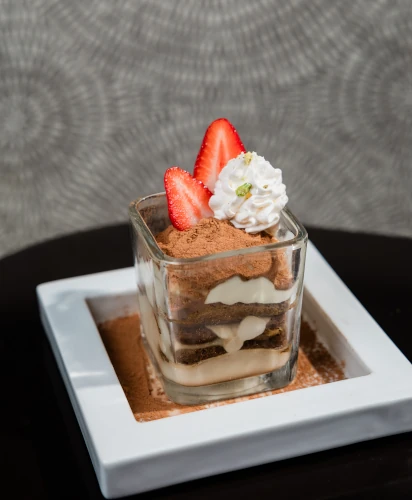 Che Vita's Tiramisu Semifreddo in a glass garnished with strawberries and whipped cream.