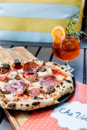 A table with Che Vita's Fratelli pizza and a cocktail garnished with an orange.