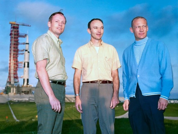 Three astronauts in front of a rocket. 