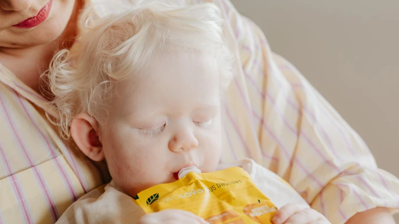 Baby feeding from plastic food pouch