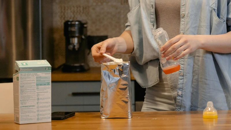 Mither scooping baby formula into a bottle.