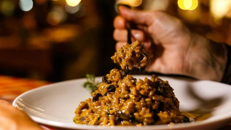 Close-up shot of rich mushroom risotto being served in a cozy restaurant atmosphere.