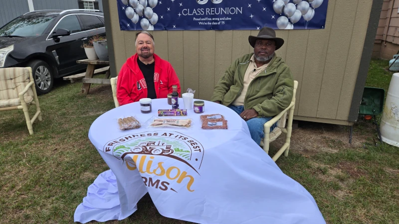 Two men pose for a picture at a product table.