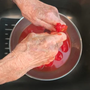 Woman squeezing tomatoes by hand over a bowl.