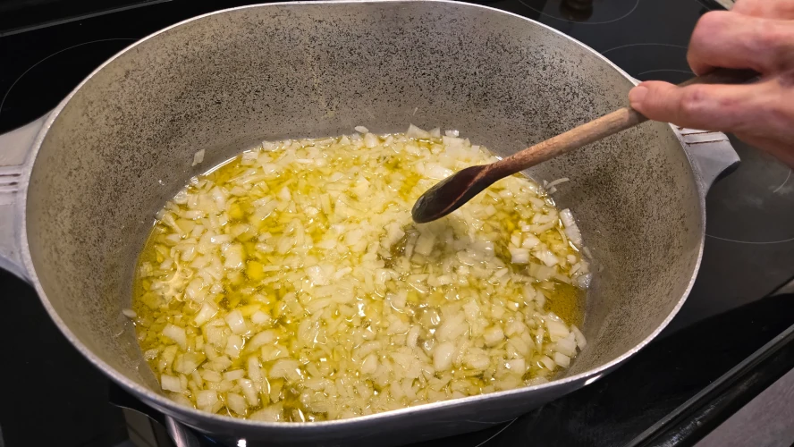 A step in the process of making pasta fazool, a woman stirs minced onion as it cooks in olive oil.