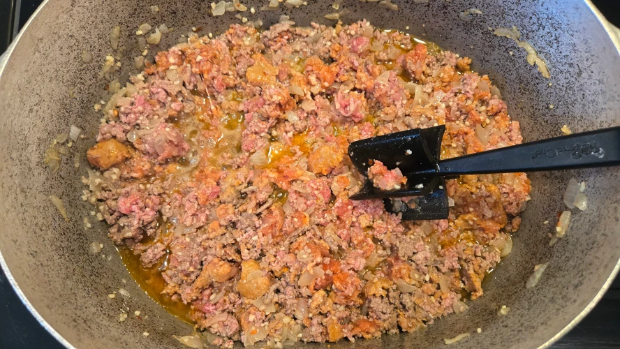 A step in the process of making pasta fazool, ground meat is chopped up in a pot.
