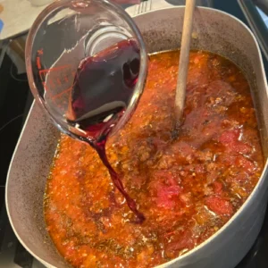 A step in the process of making pasta fazool, a woman pours red wine into pot.