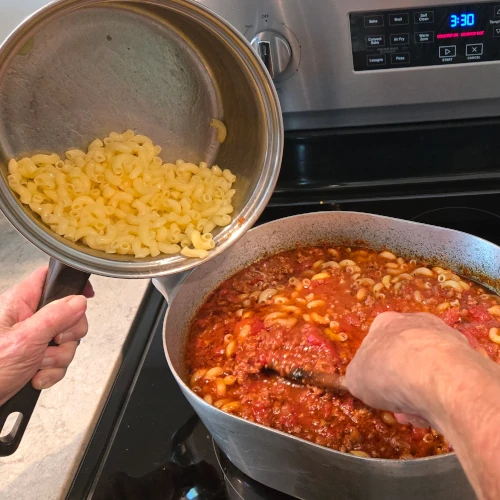 A step in the process of making pasta fazool, a woman adds boiled noodles to the pot.