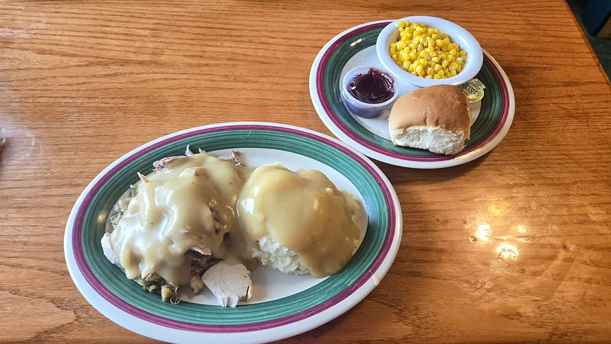 Roast turkey dinner with stuffing, mashed potatoes and gravy, served with corn, cranberry sauce and a dinner roll.