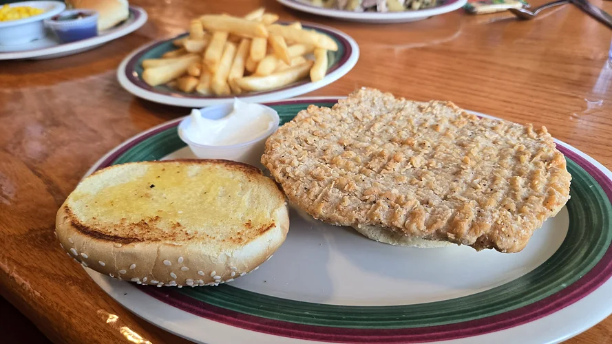 Breaded tenderloin sandwich on a toasted sesame seed bun with mayonnaise and a side of French fries.
